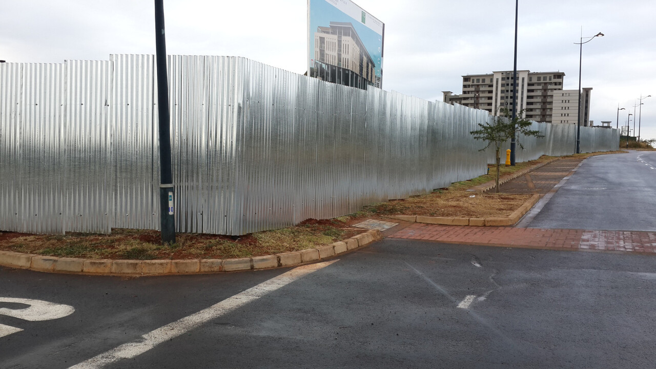 Site hoarding built from galvanised roof sheeting on a steel frame.